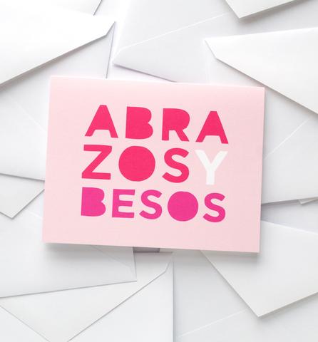 Pink card reads "Abrazos Y Besos"